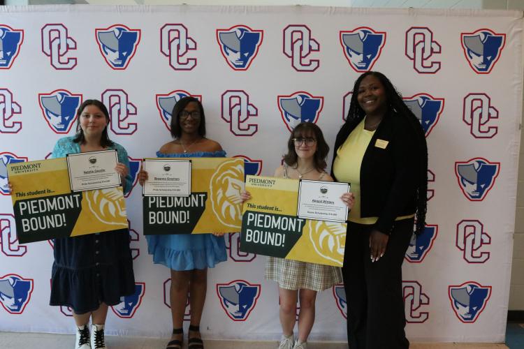Natalie Goodin (from left), Breanna Gresham and Abigail Winters display Piedmont banners with Piedmont University undergraduate admissions adviser Brittany DeVane during the OCHS Senior Honors Night in the cafeteria on Tuesday. Goodin and Gresham were awarded the Pride Scholarship, and Winters was awarded the Dean’s Scholarship.  (Photo/Anna Izquierdo)