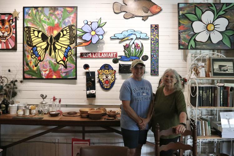 Rowdy Rooster co-owners Jamie Lewis (left) and Kathleen deMarrais stand next to Marisa Mustard’s hanging art display. The display is Mustard’s first exhibit inside the cafe. (Photo/Anna Izquierdo)