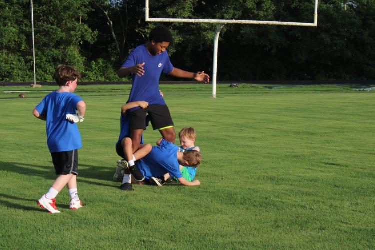 Campers attempt to wrestle student coach Keyvon Gresham to the ground before lining up for a 7v7 game at the youth football camp. The players worked on various drills before playing 7v7 games. (Photo/Elizabeth Kim)