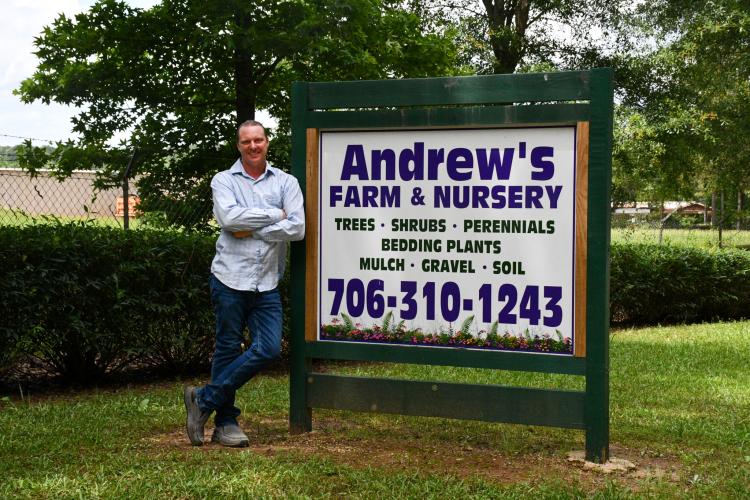 Andrew Majsztrik stands next to his welcome sign at Andrew’s Farm &amp; Nursery in Arnoldsville. The sign, designed by Letter It in Lexington, leads to the 65 acres of land Majsztrik uses for his businesses. (Photo/Jennifer Xia)