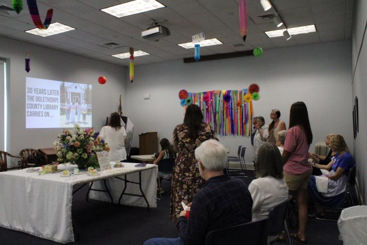 Attendees of the Oglethorpe County Library's 30th anniversary party watch a slideshow put together by branch manager Nicole Hensley. The presentation was focused on the efforts and accomplishments from the library's past and present. (Photo/Elizabeth Kim)