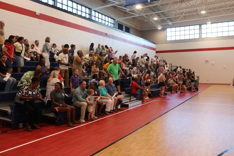 Residents and school staff gather in the new OCES gymnasium for a brief program prior to the ribbon cutting and tours of the building last Sunday. The school opened to students in January, but the construction was finished this summer. (Photo/Anna Izquierdo)