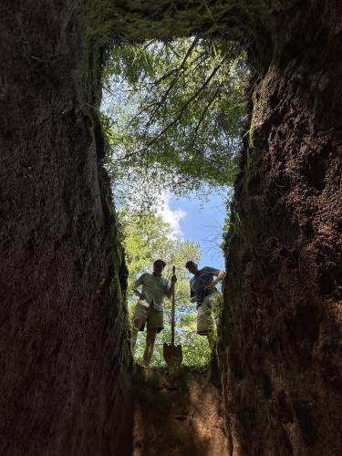 Lexington artist Terry Rowlett (left) and Dan Fortuna (right), the brother of John Fortuna, look down on John as he tests out his final resting place. (Submitted Photo)