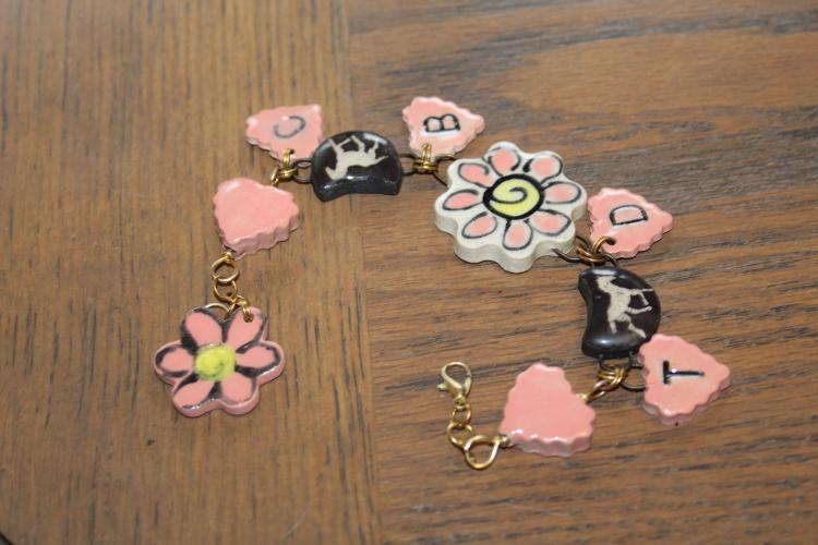 Two ceramic flowers, ceramic horse pieces and several pink ceramic hearts made by Tracy Massey are chained together to form a handcrafted ceramic story bracelet on Aug. 28, 2025. The bracelet is one of Massey's newest ceramic creations, featuring her "story" by having her, her husband and her son's initials. (Photo/Emily Adams)