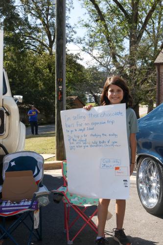 10-year-old Sophia Marchette of Lexington holds up a sign announcing her chocolate sale at the Firefly Cruise-In in Lexington, Georgia on Sunday, Sept. 28, 2025. Marchette is raising $300 for an upcoming trip to Jekyll Island with her family. (Photo/Susanna Johnson)