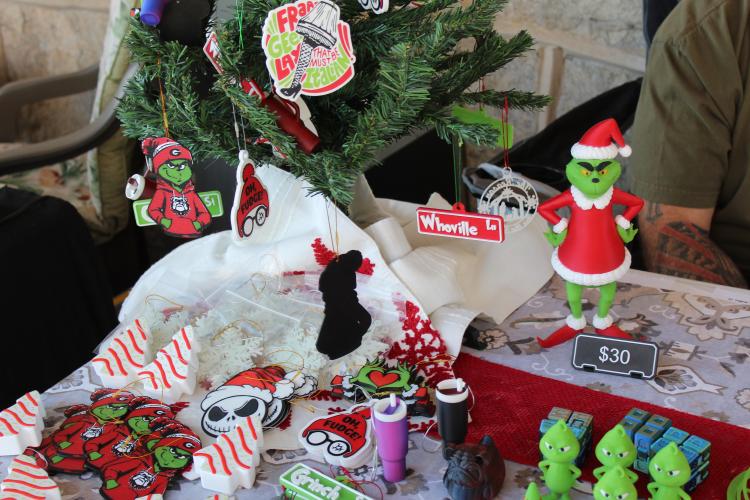 The table for Watkins in 3D, run by Nicole and Brandon Watkins, is filled with Christmas pieces they created using a 3D printer. Brandon said the Grinch figurine is the most difficult piece to print, taking 12 hours and requiring assembly in multiple parts. (Photo/Emily Adams)