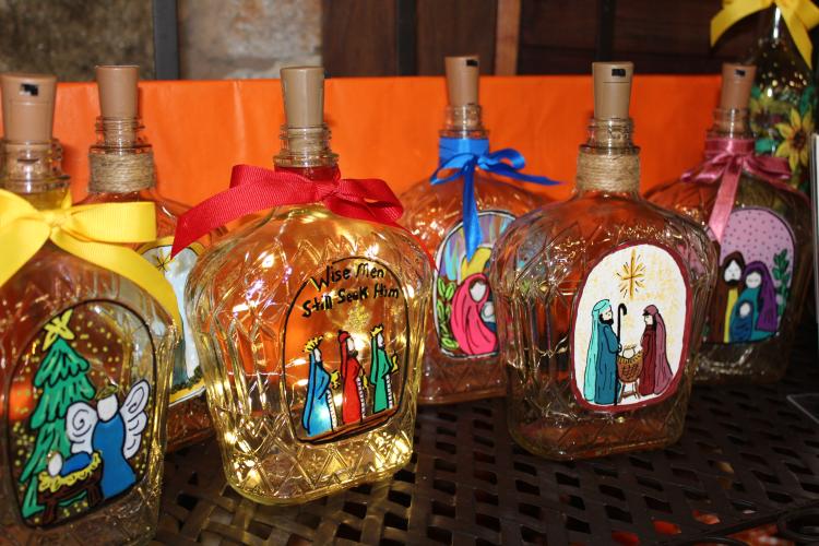 Christmas-themed, hand painted glass bottles with lights inside are part of Debbie Winsett’s booth, Light Up Your Life, at the Christmas Marketplace on Sunday, Nov. 23, 2025, at the Crawford Depot. The time it takes Winsett to paint each bottle varies, and she painted three before coming to the marketplace on Sunday. “I love seeing the people come through, meeting people I've never met before,” Winsett said. “I just I love that, I just love the atmosphere.” (Photo/Emily Adams)