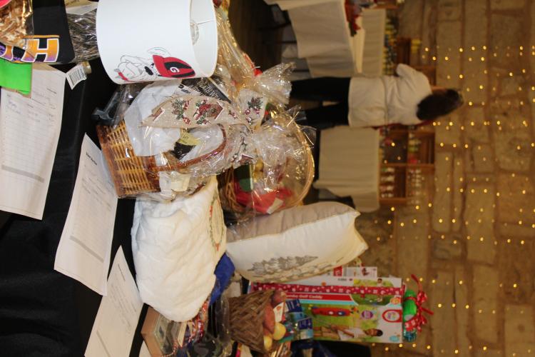 The silent auction table is filled with items, some donated by vendors, inside the Crawford Depot at the Christmas Marketplace on Sunday, Nov. 23, 2025, at the Crawford Depot. One of the vendors, Debbie Winsett, hand-painted a Georgia Bulldogs lampshade that she donated to the auction. The auction is held on Sunday, and proceeds benefit the Oglethorpe County Chamber of Commerce. (Photo/Emily Adams)