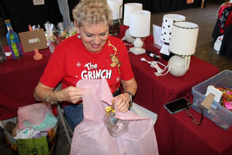 Debbie Winsett wraps a holiday-themed, hand-painted glass bottle she made and sold at her booth — Light Up Your Life — at the Christmas Marketplace at the Craw- ford Depot on Sunday. Winsett also sold hand-painted University of Georgia pieces that were sold out by the last day of the marketplace. “I call myself ‘Light Up Your Life,’ because most of the things that I do — all of my bottles — light up,” Winsett said. “I started painting lamp shades, and they all light up.” (Photo/Emily Adams)