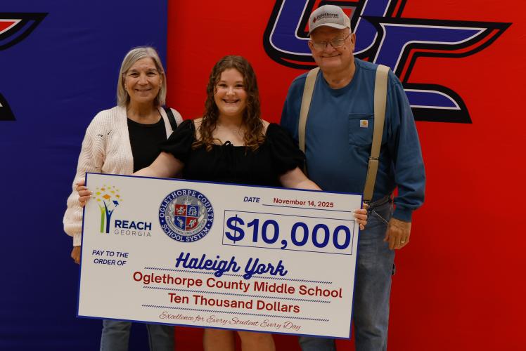 Haleigh York stands with her grandparents while holding her REACH Georgia Scholarship check at Oglethorpe County Middle School on Friday, Nov. 14, 2025. York plans to attend Athens Technical College to pursue nursing, a goal her family proudly supports. (Photo / Drew Bearden)