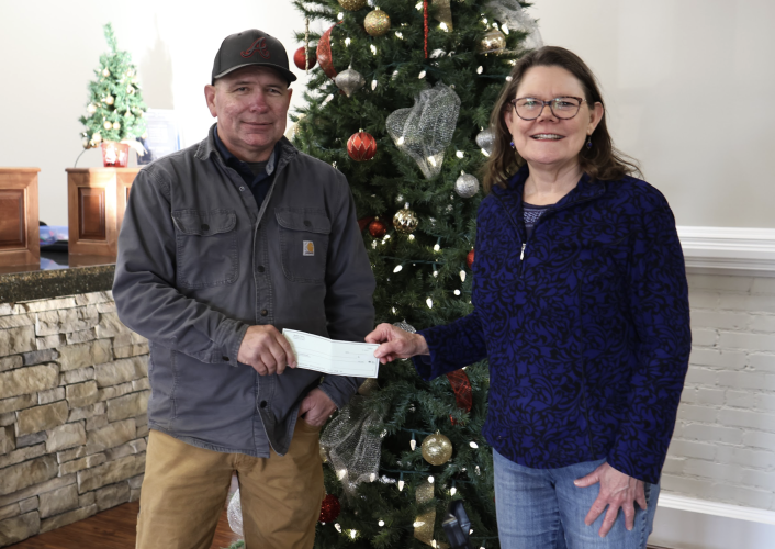 Catherine Bowen Drewry, founder and co-chair of Community Christmas, accepts a donation from Jason Robertson in The Commercial Bank on Monday. Robertson works at Johnson &amp; Johnson, which donates $5,000 annually to Community Christmas through its outreach program. (Photo/Katherine Davis)