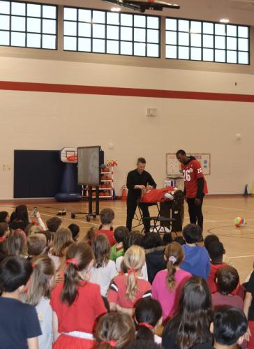 Malcolm Mitchell, author and former NFL athlete, helps Ken Scott, magician, set up a levitation trick with third grade student volunteer Hazelynn Walton, on Feb. 4, 2026. Students watch amazed as Walton levitates from the back of a chair. (CHARLOTTE COCHRAN/THE OGLETHORPE ECHO)