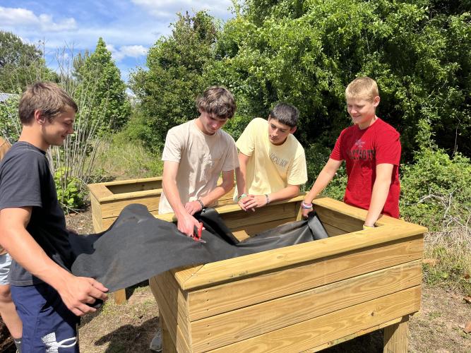 Paul Pittard (from left), John Brown, Will Weaver and Kaleb Butler cut landscaping fabric to place inside the garden boxes to help keep the soil from falling out at the Oglethorpe County Senior Center on Tuesday. (Photo/Emilie Sullivan)