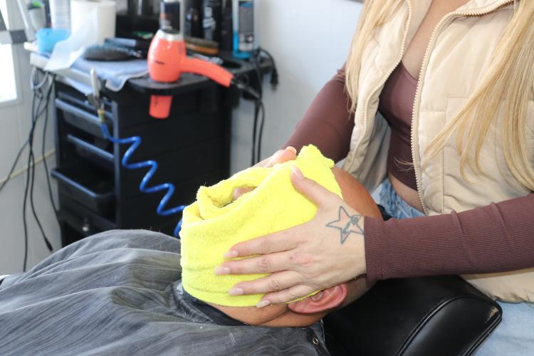 Mandi Kirk demonstrates part of a straight razor beard service, placing a hot towel on Ron Whitehead's face to help open pores. She said attention to detail — including the use of hot towels — is what sets a good haircut apart from a quick one. (Photo/Emilie Sullivan)