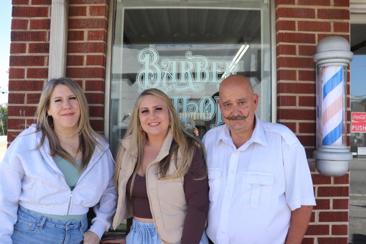 Lucy Misenhamer (from left), Mandi Kirk and Ron Whitehead stand in front of Oglethorpe Barbershop in Crawford this spring. Kirk opened the shop four years ago and cuts hair along with Misenhamer and Whitehead. (Photo/Emilie Sullivan)