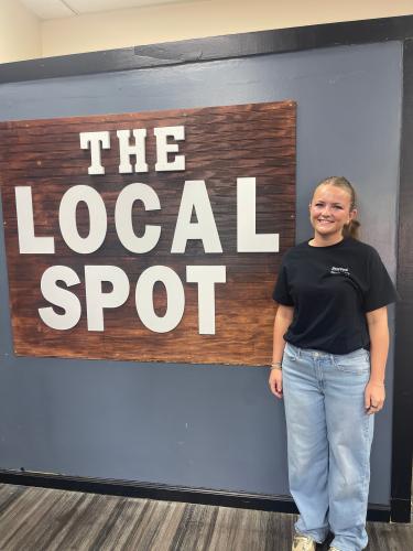 Sofia Horsley, a front-of-house employee at The Local Spot, stands next to a sign with the restaurant's name on Friday morning during the location's grand opening. Horsley said some of her favorite menu items are the lemon pepper wings, onion rings and loaded fries. (Lexie Shadix/The Oglethorpe Echo)