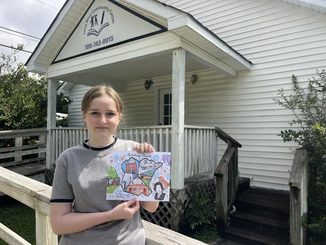 OCHS student Maeve Haydock, who is 15, holds a draft of her mural design in front of the Lena Wise Community Center. Haydock’s mural will be on a wall inside the center and contain images relating to Oglethorpe County. (Sarah Nanos/The Oglethorpe Echo)