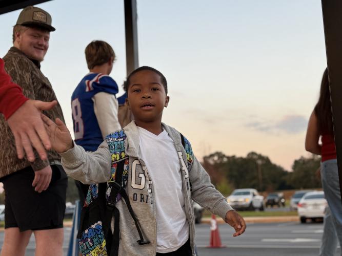 An OCES student high-fives OCHS football player Jake Huff at the Patriot Pride drop-off line. “For the players, it gives them a sense of pride,” said Campbell. “It makes them, you know, to these little kids, their heroes, their hometown heroes.” (Photo/Walker Durham)