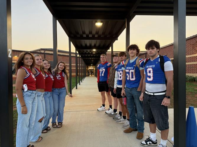 [Left to Right] Cheerleaders: Malia McCalla, Jenna Harvey, Ava Hughes and Dulciana Miranda, and OCHS football players Jake Huff, JD Armour, Justin Wilson, Lance Ellefson and Coleton Sexton pose along the entryway leading into the OCES building. The students try to arrive around 7:25 a.m. on Friday mornings and greet the kids until the morning announcements begin. (Photo/Walker Durham)