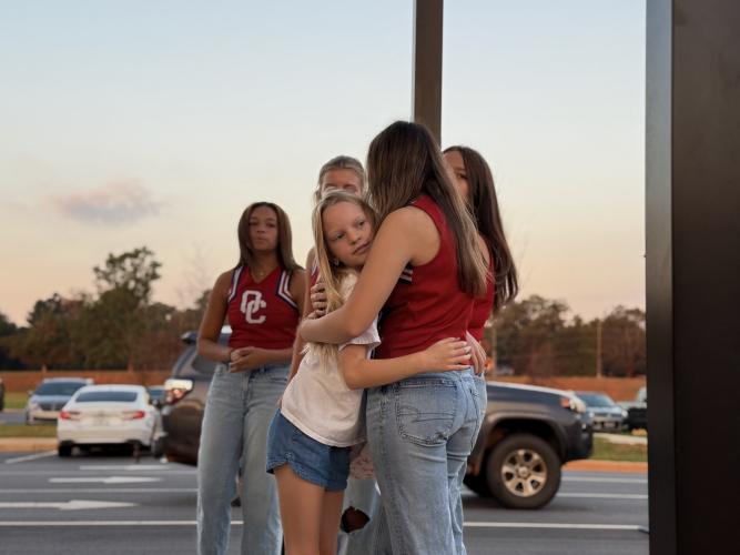 OCHS Cheerleader Dulciana Miranda hugs an OCES student at the Patriot Pride Drop-off line. “I remember wanting to be them [cheerleaders], so it’s so cool, like, actually, like, being them,” said Miranda. (Photo/Walker Durham)