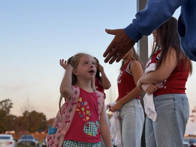 An OCES student looks up at OCHS Defensive Coordinator Mike Campbell as she winds up her high-five. Campbell was a part of the tradition when he was a football player at the school, and he, along with Janine Campbell and the Athletic Booster Club, was inspired to reignite the tradition for the next generation of players and kids. They met with the OCES administration and the cheerleading coaches to bring the drop-off to life. (Photo/Walker Durham)