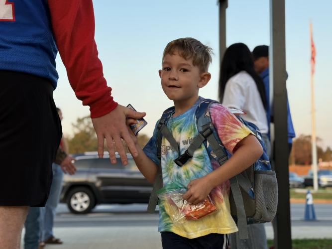 An OCES student high-fives football player Jake Huff while holding a bag of snacks and a Pokémon card. The kids are greeted by the players and cheerleaders right as they step out of the car every Friday morning. (Photo/Walker Durham)