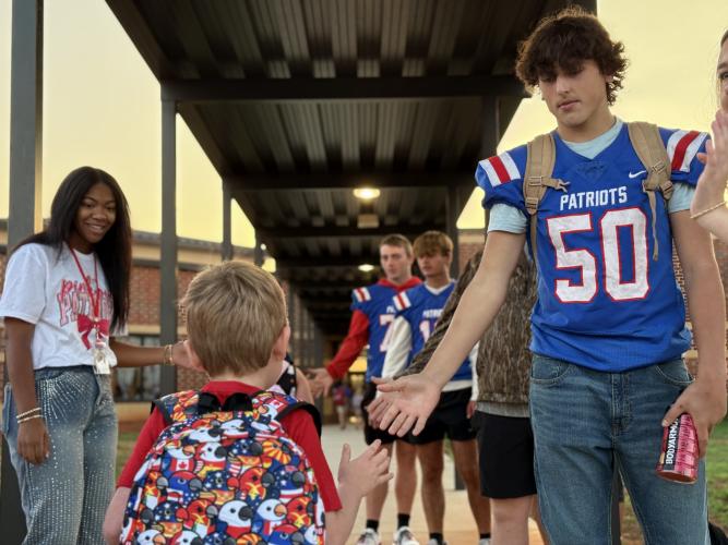 OCHS football player Lance Ellefson prepares to high-five an OCES student as they walk through the patriot pride line. ”For the players, it gives them a sense of pride,” said Janine Campbell, President of the Athletic Booster Club. It makes them, you know, to these little kids, their heroes, their hometown heroes.” (Photo/Walker Durham)