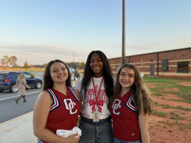OCHS cheerleaders Ava Hughes, Dulciana Miranda and  Neveah Calhoun pose together at the patriot pride drop-off line. The cheerleaders have felt the impact the greeting has had on them. “It feels even better whenever, like, you’re standing there, and, like, a random kid just comes up to you and hugs you, and they recognize you,” said OCHS cheerleader Ava Hughes. (Photo/Walker Durham)