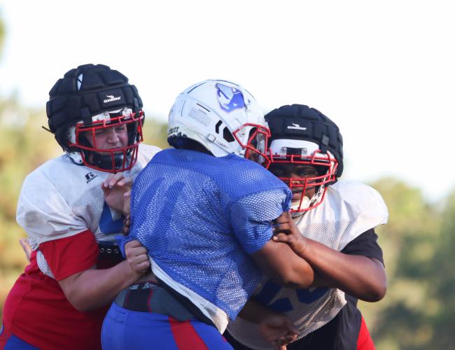 Sophomore Kayden Phelps (left) and junior Isaiah Hood block a teammate during Oglethorpe County football practice earlier this season. Phelps and Hood are wearing Guardian Caps, which have been shown to help prevent concussions. (Sydney Jarrard/The Oglethorpe Echo)
