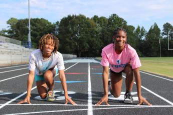 Sydnie (left) and Kenzie Henderson smile as they show off their track starting positions. The fraternal twins are star athletes in several sports at Oglethorpe County, including volleyball, cross country, basketball and track. (LAUREN HILL/THE OGLETHORPE ECHO)