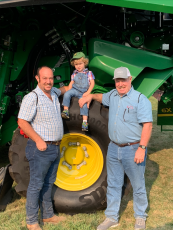 Ben Brubaker (from left), his son Benji and his father Dale gather around the wheel of a combine. The Brubaker family, which grows crops on their farm on Comer Road, could see a third generation of farmers if Benji decides to continue the tradition. (Submitted photo)
