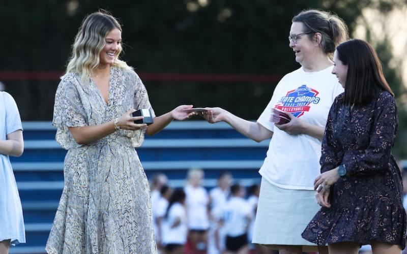 Senior Elizabeth Cook, the Class A state championship tournament MVP, accepts her state title ring from coach Brianne Harrison and assistant coach Toni Walser-Childs at Patriot Stadium on Tuesday night. The OCHS girls volleyball team was presented with its championship rings after winning the Class A state volleyball title in October. (Sydney Shankman/The Oglethorpe Echo)