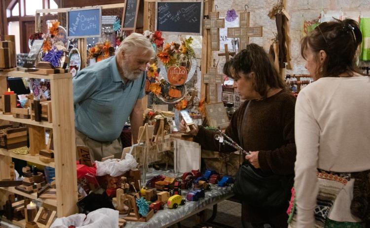 Gary Palmer talks with visitors at the Christmas Market in Crawford on Nov. 21. Palmer makes wooden toys and other items by hand and sells them with his wife, Naomi Palmer, who also handmakes decorations and items. (Photo/Sarah White)