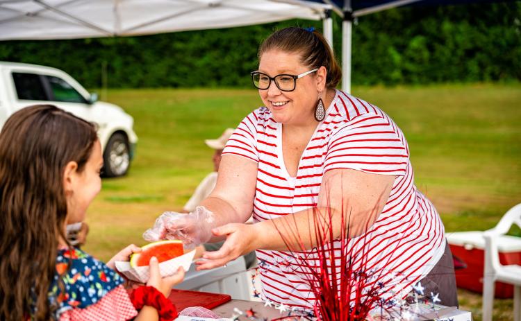 Crawford’s Heather Stevens hands out watermelon while manning the Crawford Baptist Church’s table at the Fourth Annual Independence Day Celebration at Bryan Park on Monday. (Photo/Jack Casey)