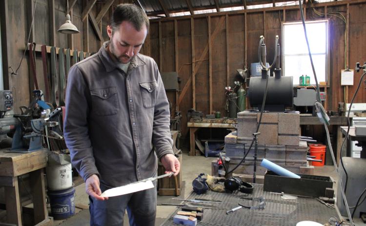 Luke Snyder holds an unfinished chef knife featuring a single bevel at Bloodroot Blades in Arnoldsville. There’s a 52-month waiting list for the knives handcrafted by Snyder and partners Katy and David Van Wyk. (Sarah Donehoo/The Oglethorpe Echo)