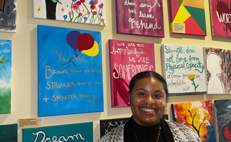 Tiara McRae, the legal advocate for Project Safe, stands in front of an art wall. The art is all created by individuals who have experienced domestic abuse and told their story at an event called Through an Open Window. (Lily Murphy/Oglethorpe Echo).